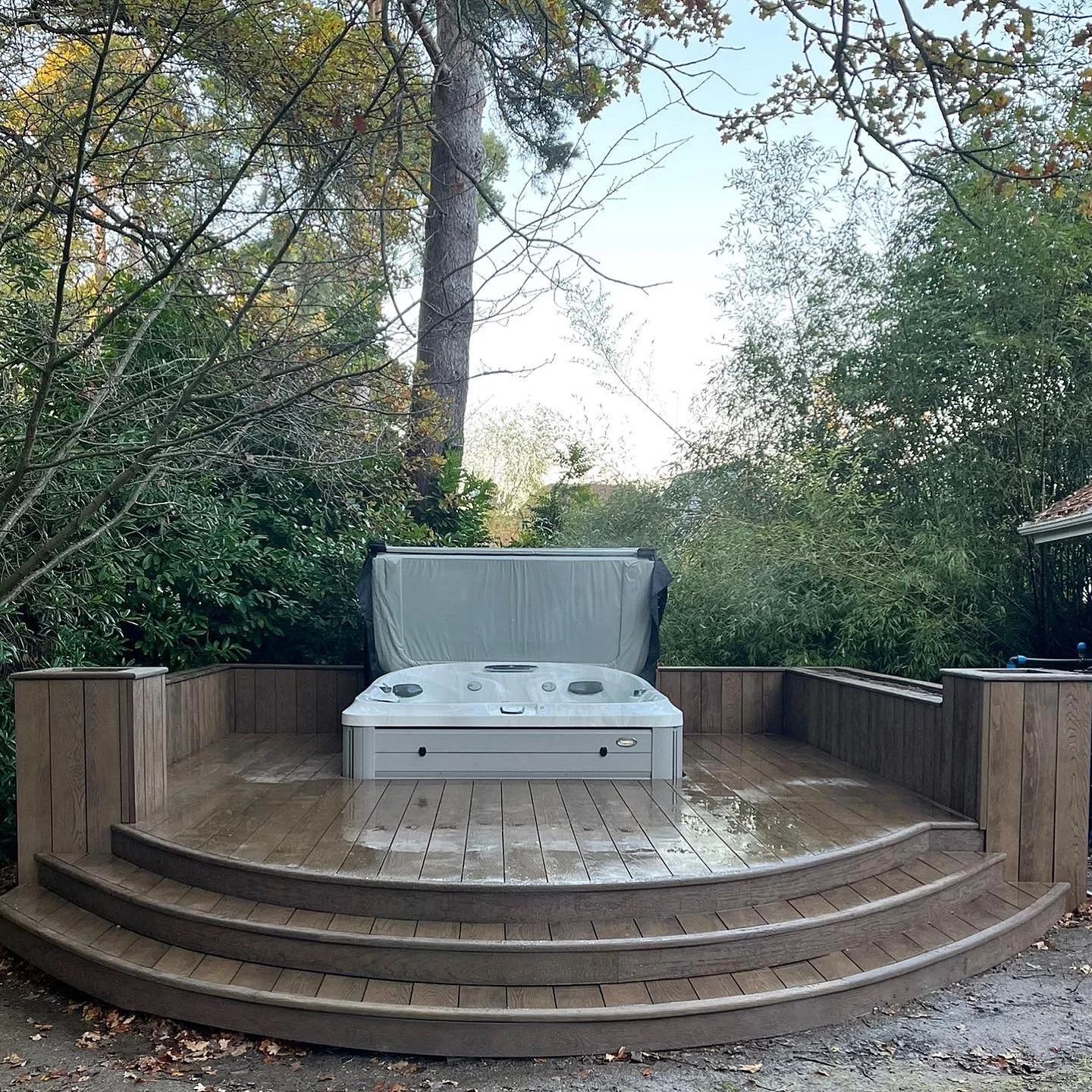 A hot tub on a wooden deck surrounded by trees and bushes.