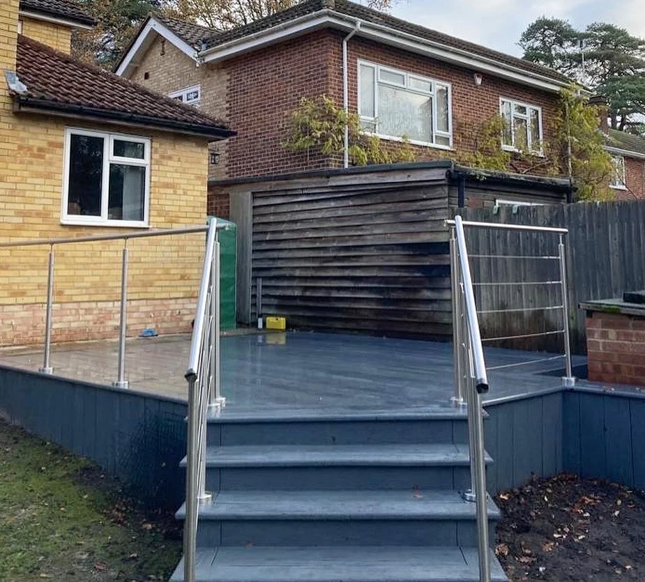 A newly installed wooden deck with metal railings and stairs, attached to a brick house with a fenced yard.