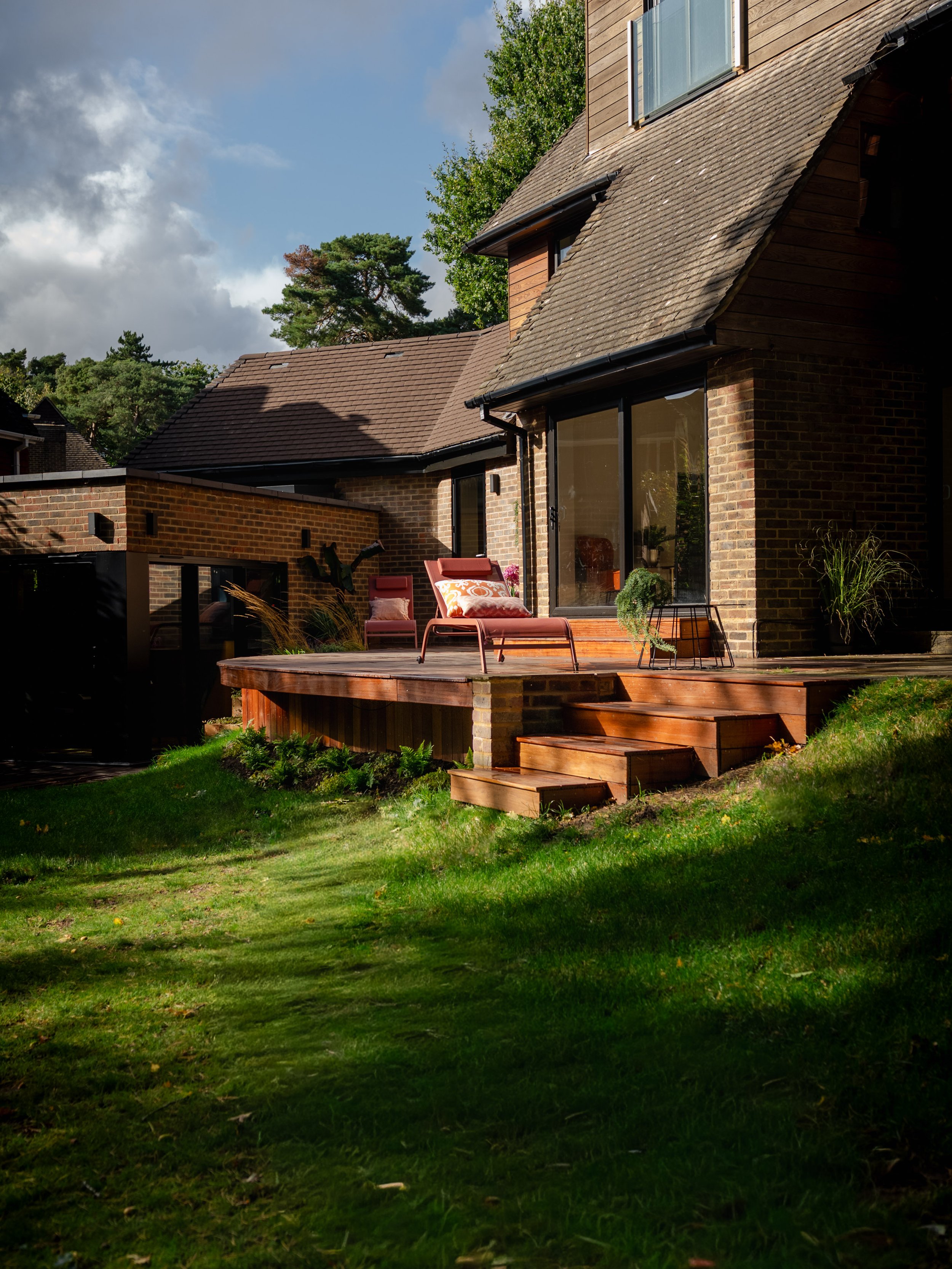 A garden patio decking with wooden stairs leading to a garden with potted plants. Expert landscapers and garden designers in Surrey, Hampshire, Berkshire, Camberley, London and surrounding areas.