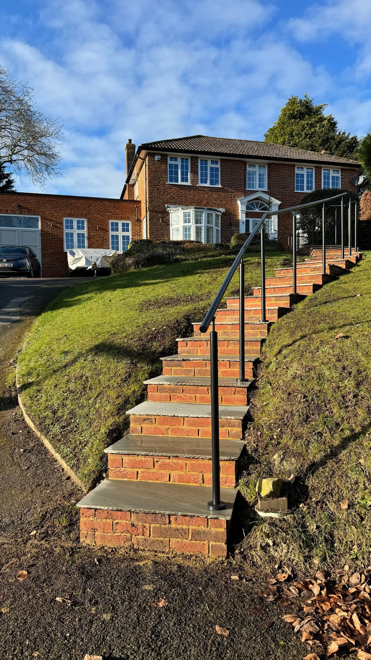 Brick staircase with a metal railing leading up to a brick house on a hill. Esme are a widely trusted garden design and landscaping company serving surrey, hampshire, berkshire, ascot, london and surrounding areas.