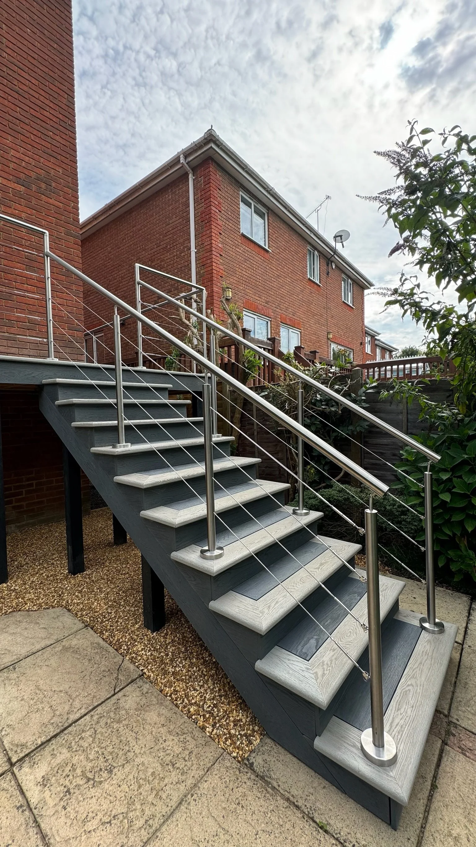 Outdoor staircase with metal railing leading to a residential building made of red brick, with multiple windows, under a cloudy sky.