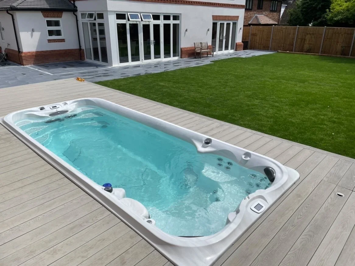 A backyard with a hot tub on a wooden deck, a grassy lawn, and a house with large glass sliding doors.