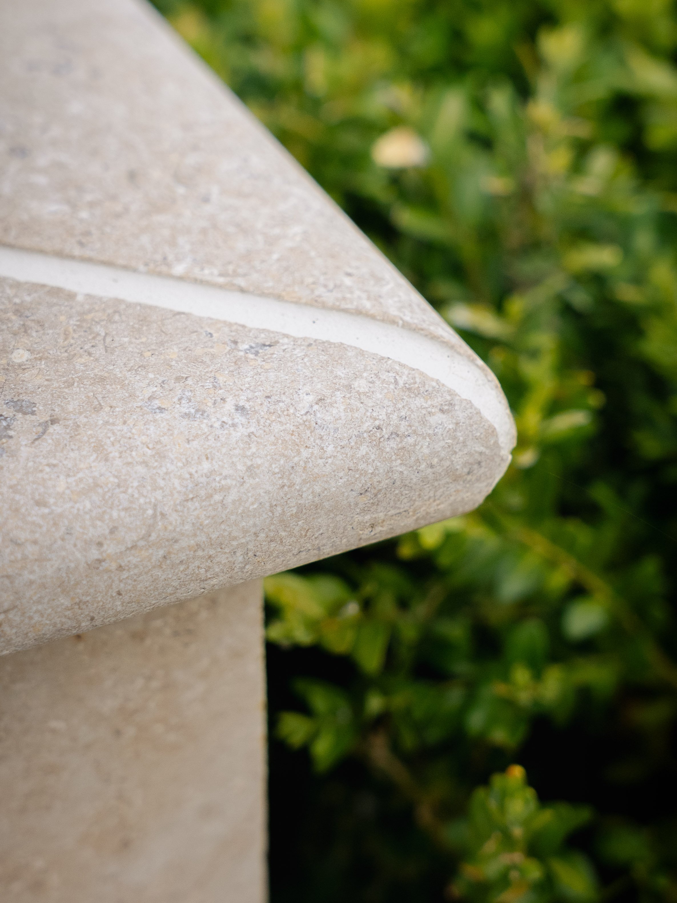 Close-up of a beige stone sculpture with rounded edges, set against a background of green foliage.