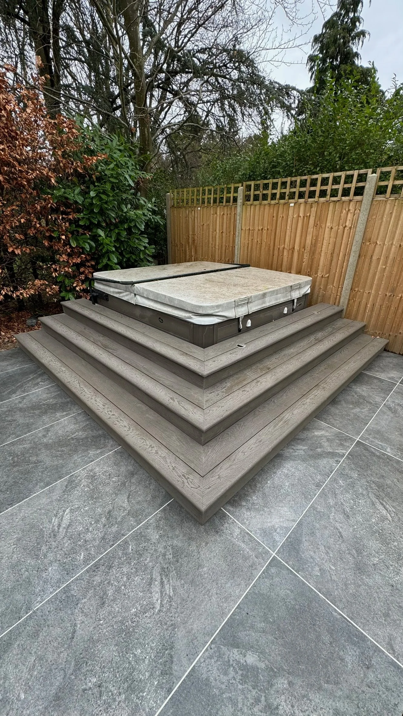 A hot tub on a raised wooden deck, with a privacy fence. Esme is a garden design & landscaping company serving surrey, hampshire, berkshire, camberley, london & surrounding areas. We build bespoke outdoor living spaces with a hot tub, swim spas, etc.