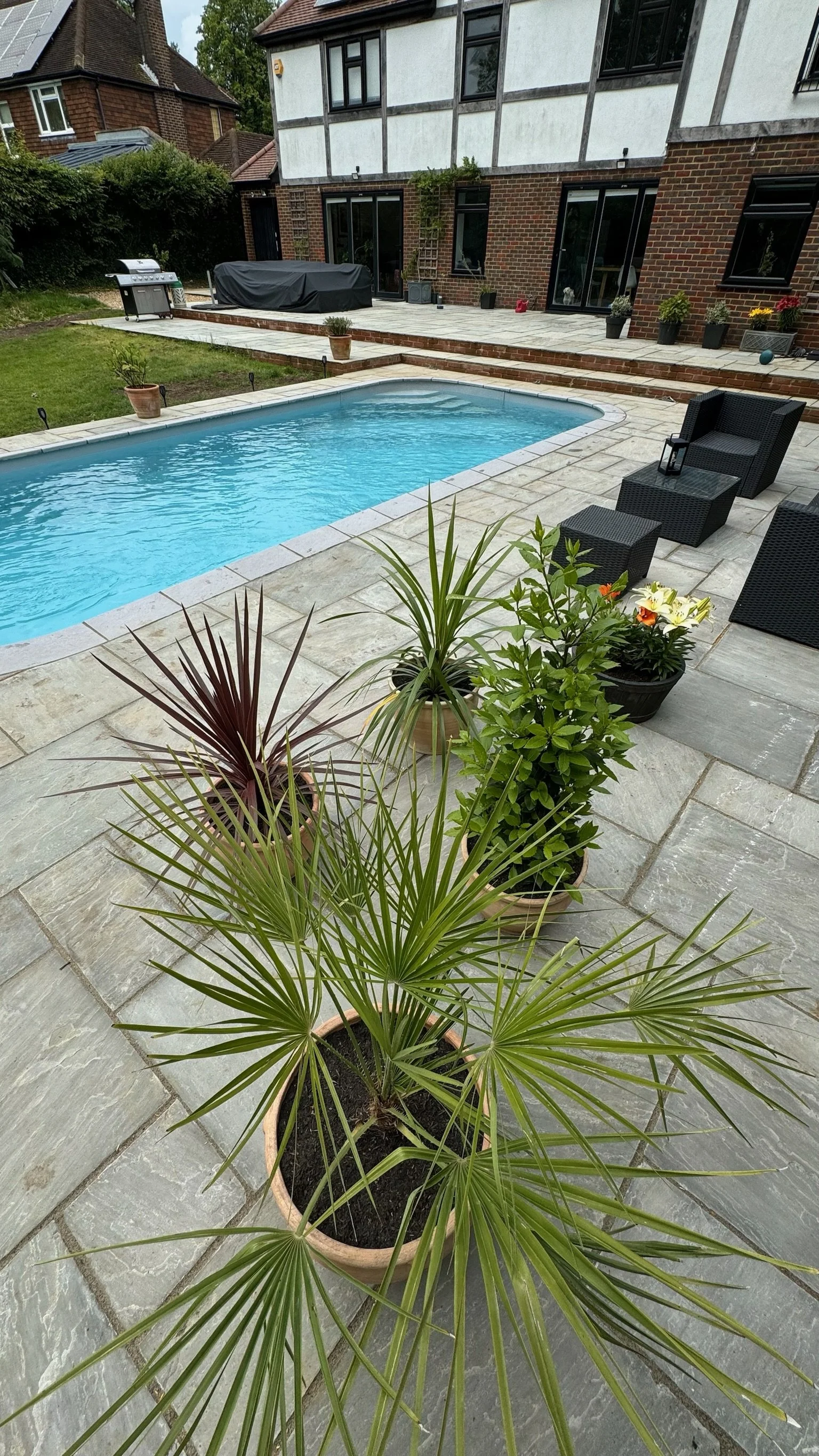 Backyard with a swimming pool, potted plants, outdoor furniture, and a covered barbecue grill.