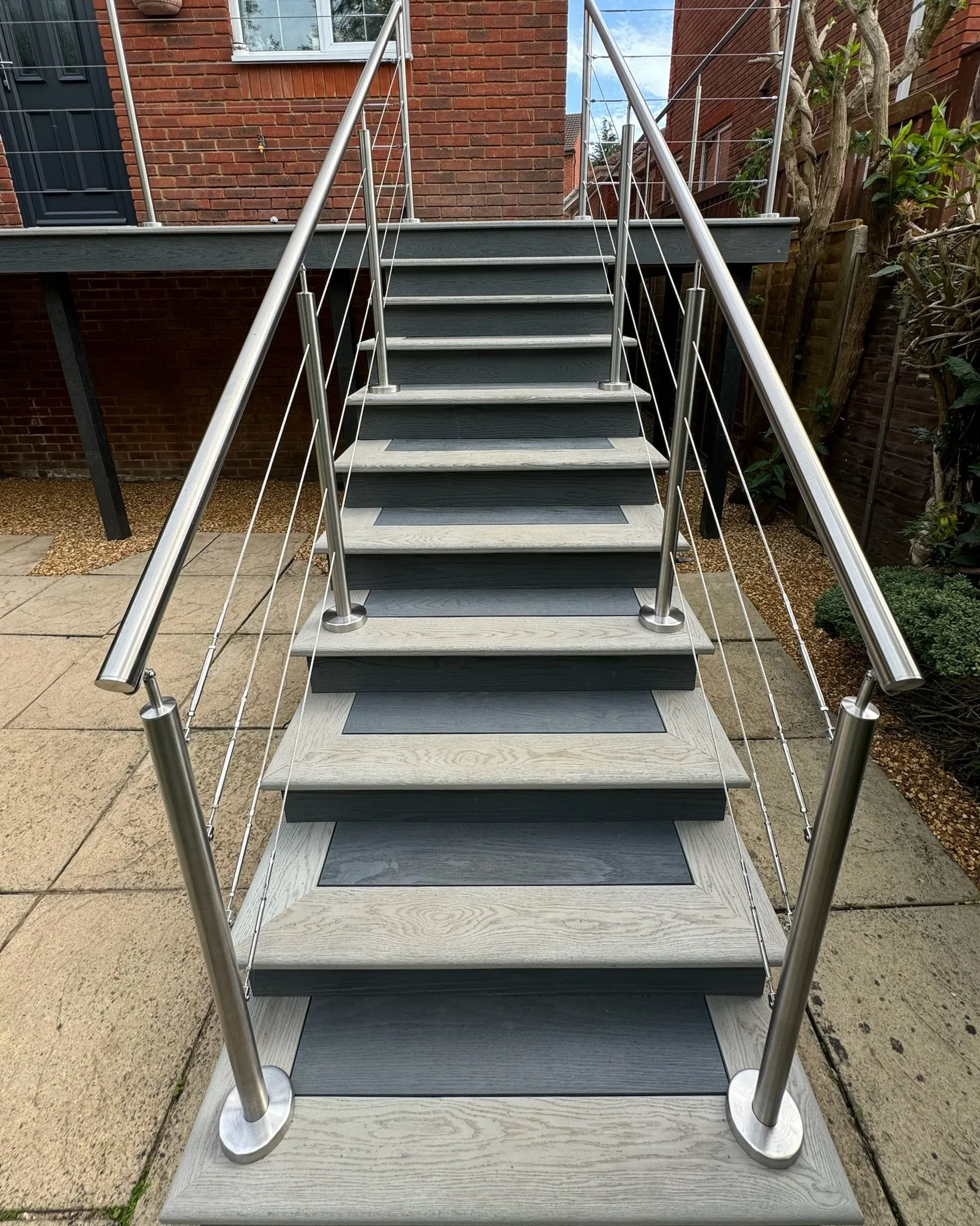 Outdoor metal railings staircase with millboard cladded steps leading up to a second-floor entrance of a brick house. Esme are a widely trusted garden design and landscaping company serving surrey, hampshire, berkshire, ascot, london.