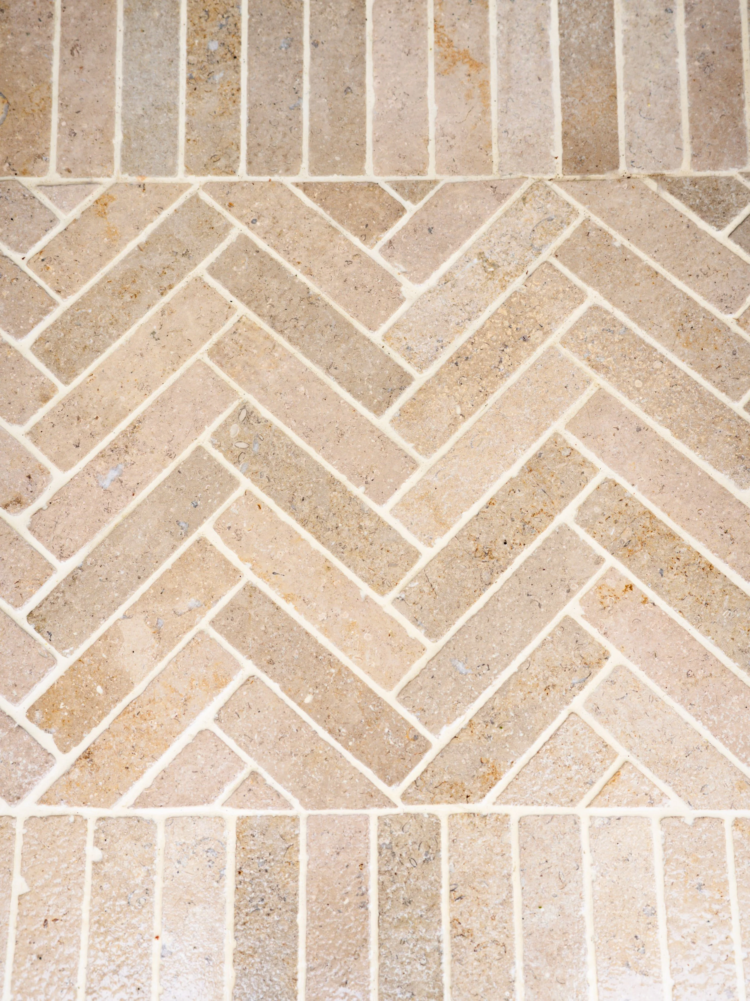 Close-up of a brick sidewalk arranged in a herringbone pattern, with an outer border of bricks laid in a straight pattern.