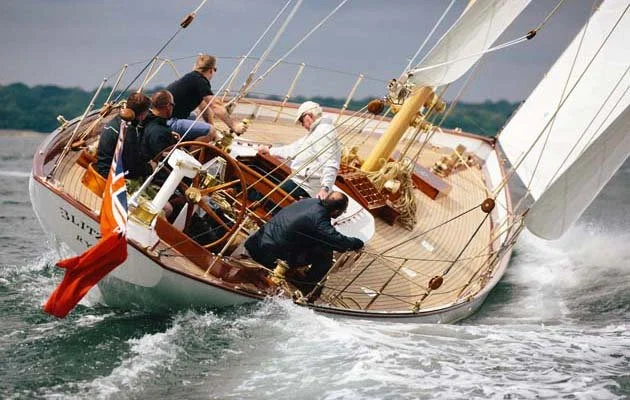 A sailing boat with multiple crew members working on adjusting sails during a race on choppy waters.