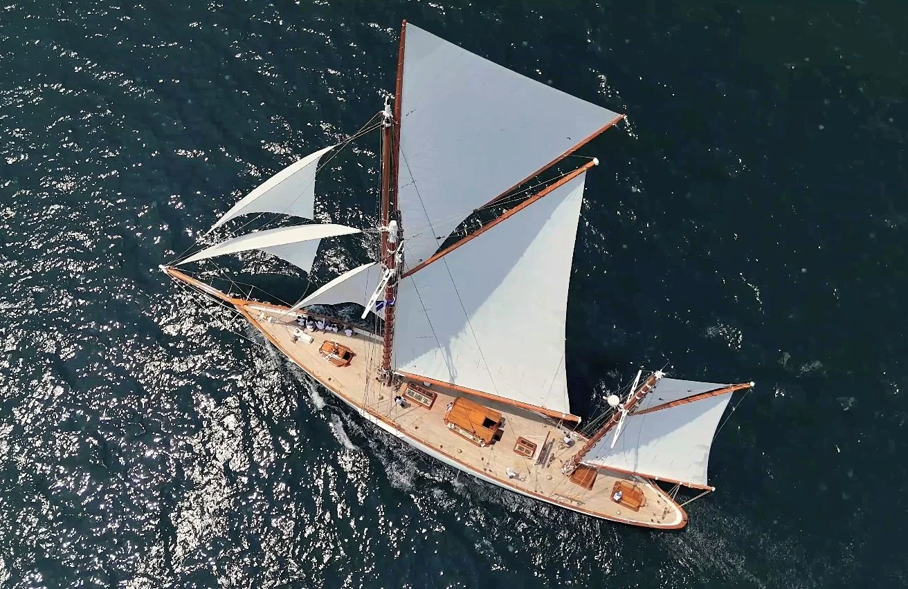An aerial view of a large sailing ship with multiple masts and white sails on open water.