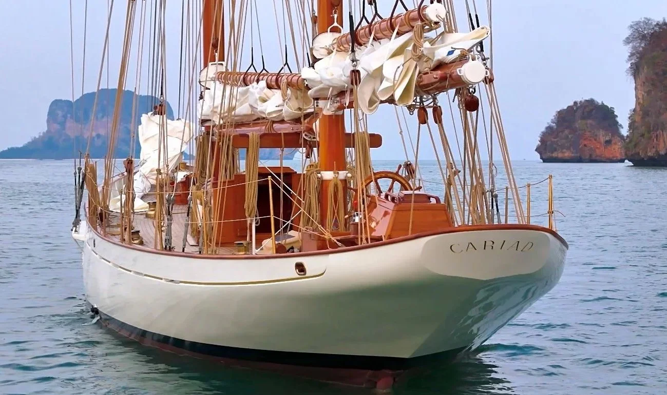 A wooden sailboat named Cariad on the water with islands in the background.