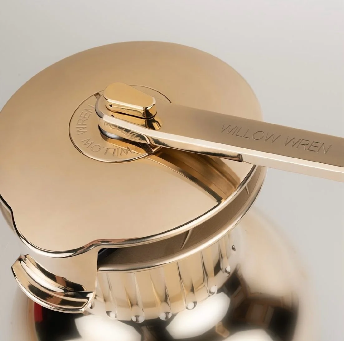 Close-up of a gold-colored coffee percolator lid with a metallic handle that has the words 'WILLOW WREN' engraved on it.