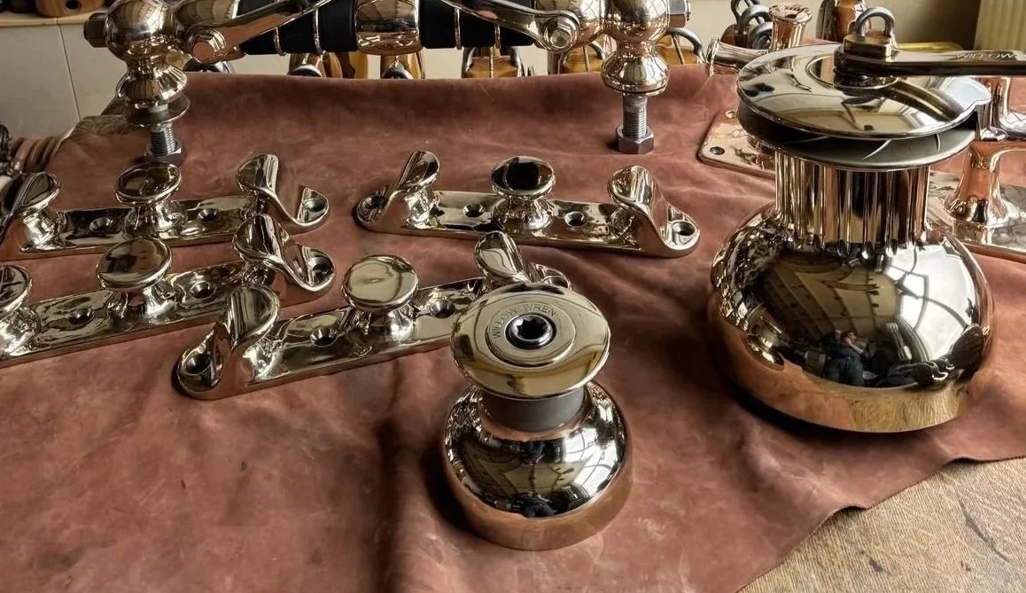 Various polished metal door handles and hardware pieces displayed on a pink fabric surface.