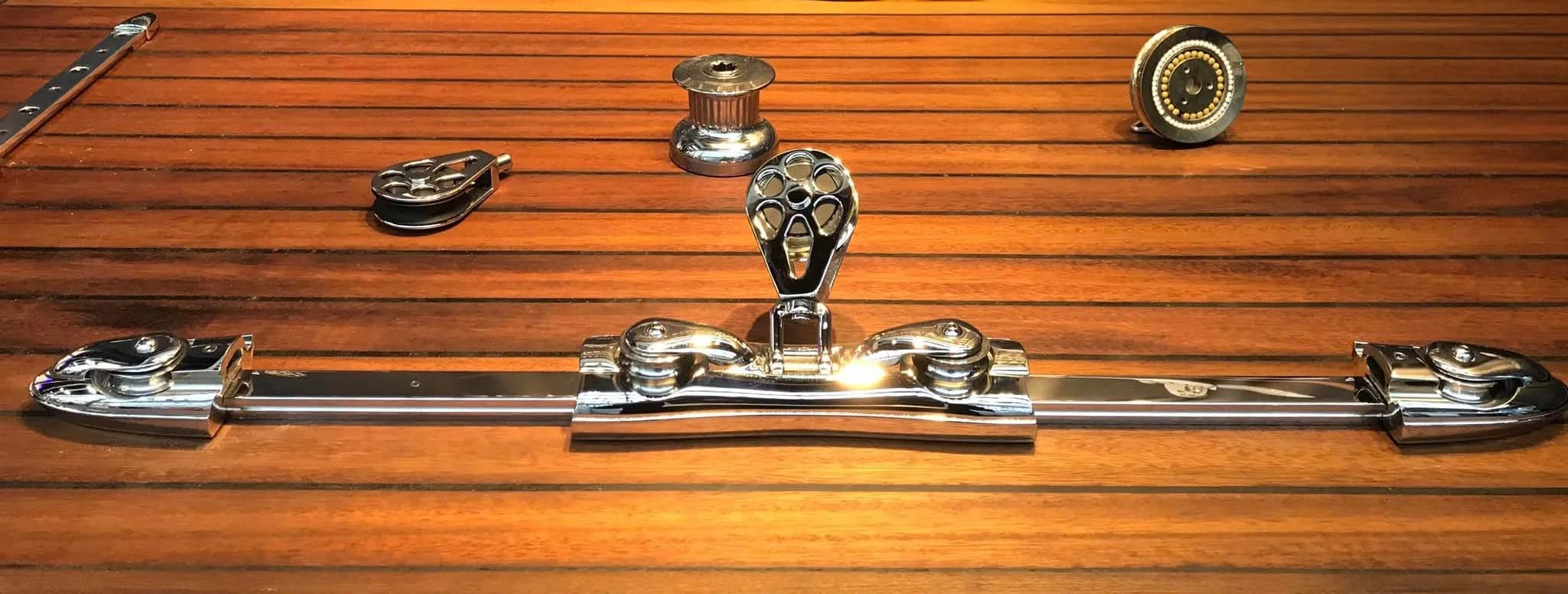 Metal sailing hardware pieces on a wooden surface, including pulleys and track fittings.