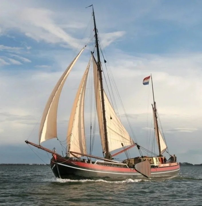 A sailing ship with multiple sails on the water, flying a flag with horizontal red, white, and blue stripes.