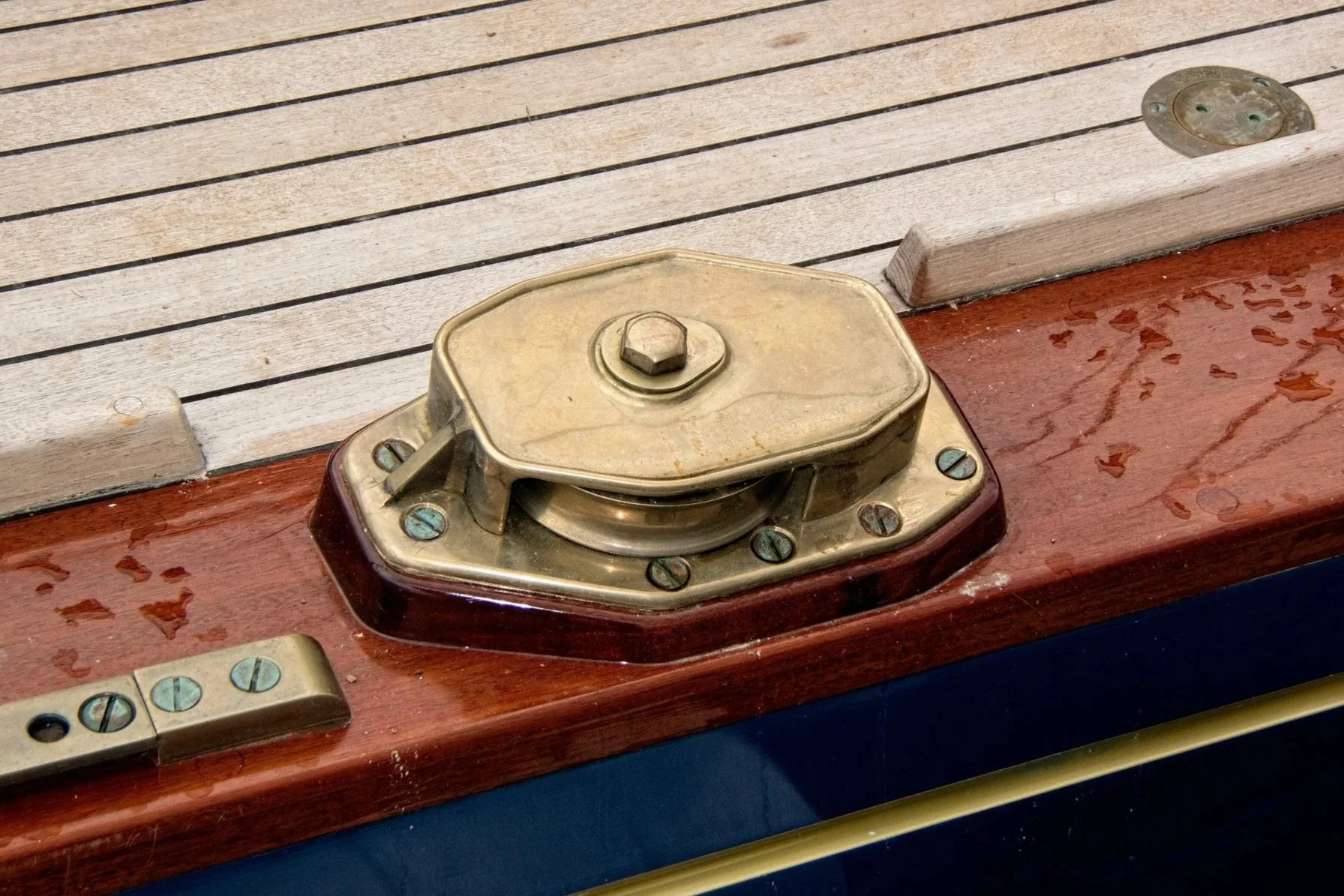 Close-up of a brass hatch cover on a wooden surface with screws and other hardware.