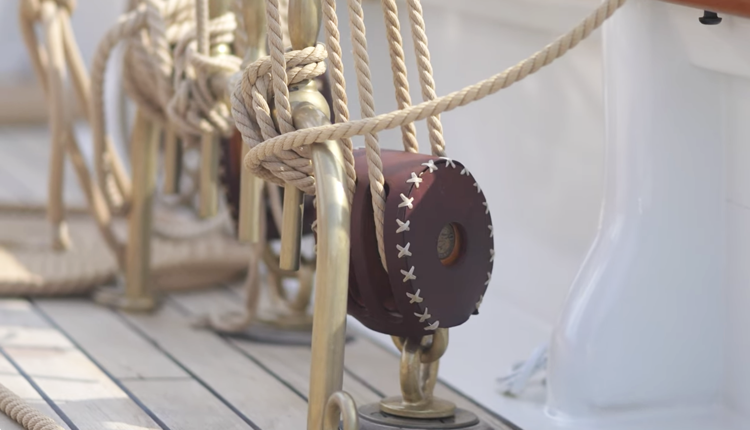 Close-up of a nautical decoration on the deck of a boat, featuring a brown leather strap with white cross-stitching, ropes, and a metal rail.