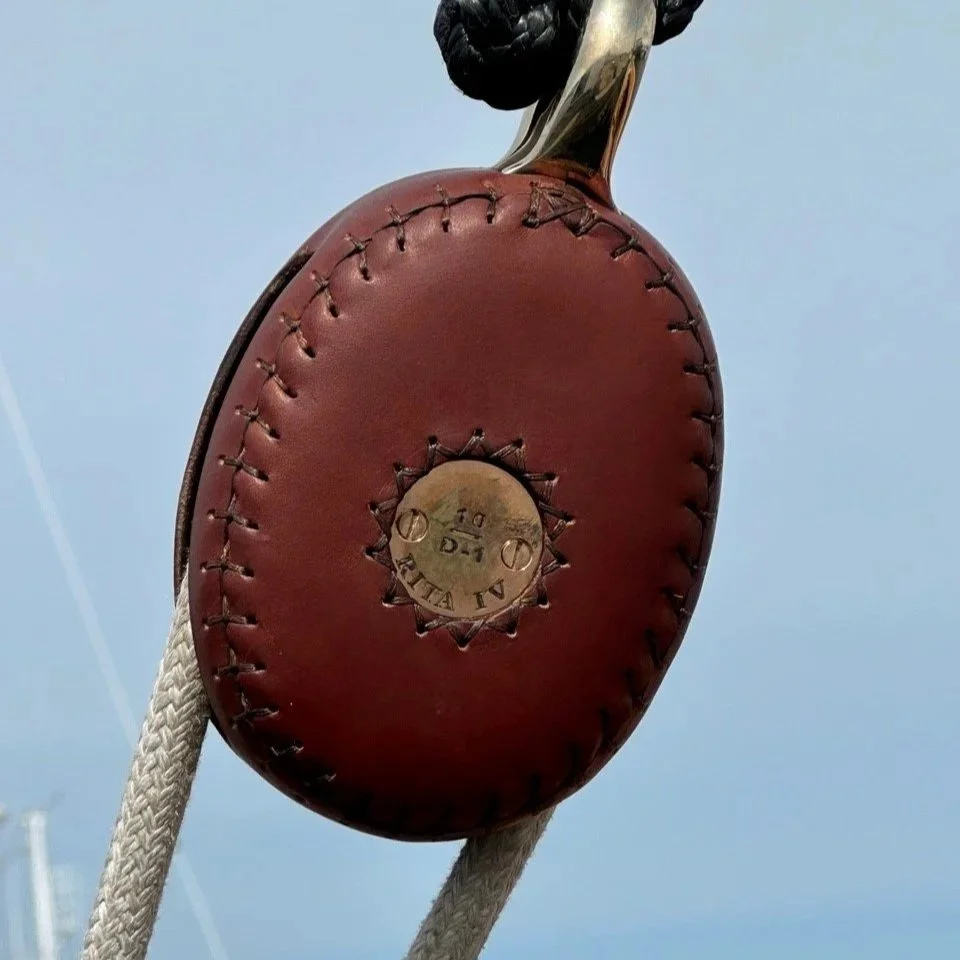 A vintage leather baseball glove with a metal tag, hanging by white ropes against a clear blue sky.