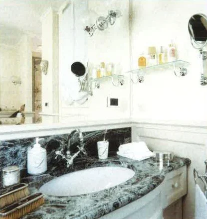 Waschbecken im Badezimmer mit grünem Marmor-Arbeitsplatte, Seifenspender, Zahnbürstenhalter, Spiegel und dekorative Gegenstände.