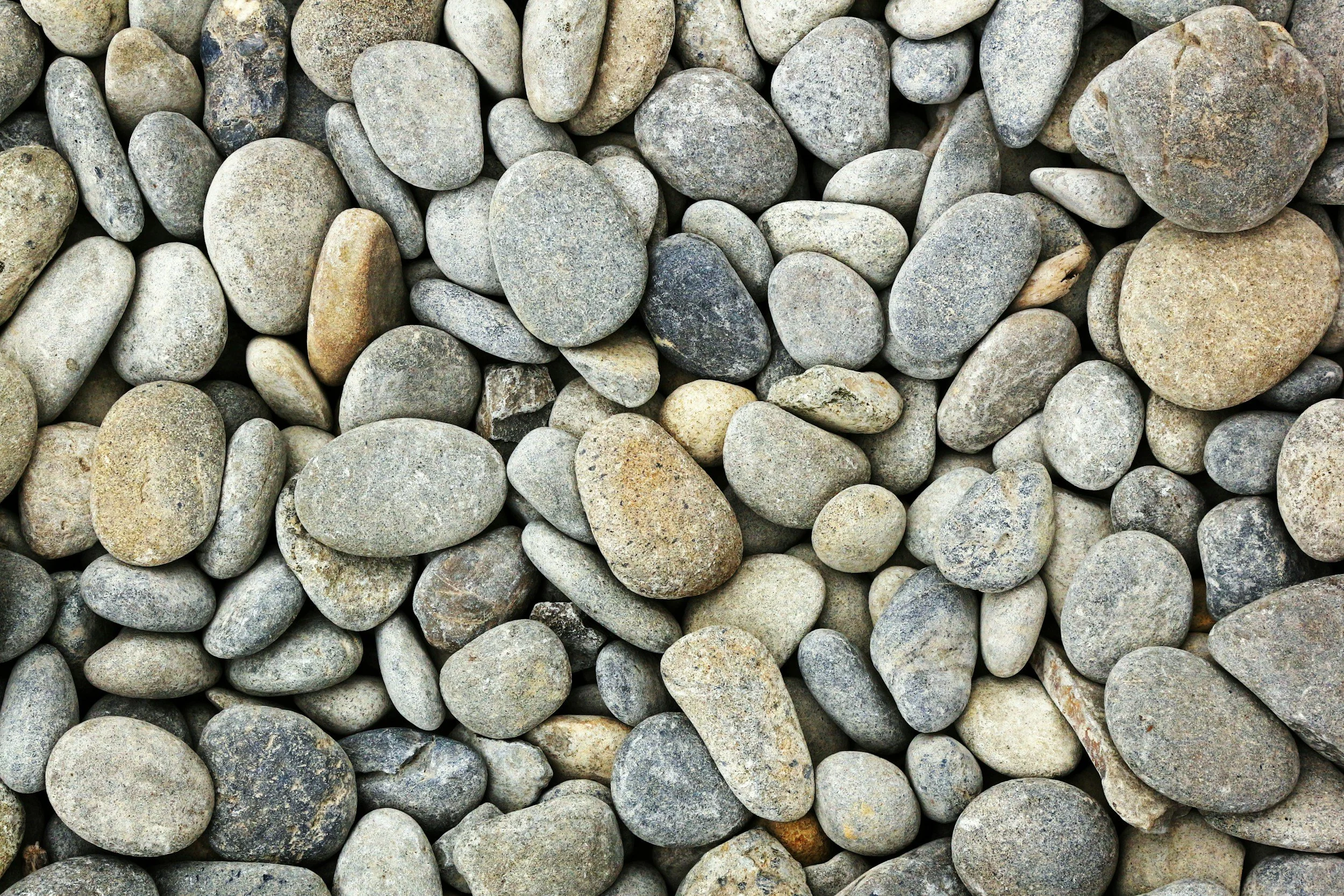 Eine Vielzahl von glatten, verschiedenen grau-braunen Steinen auf dem Boden.