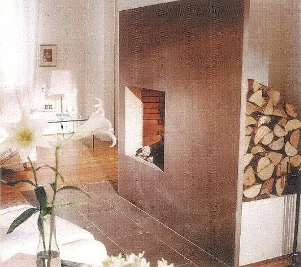 Ein Wohnzimmer mit Kamin, Holzstapel und einem Sessel, dekoriert mit einer Vase mit Blumen