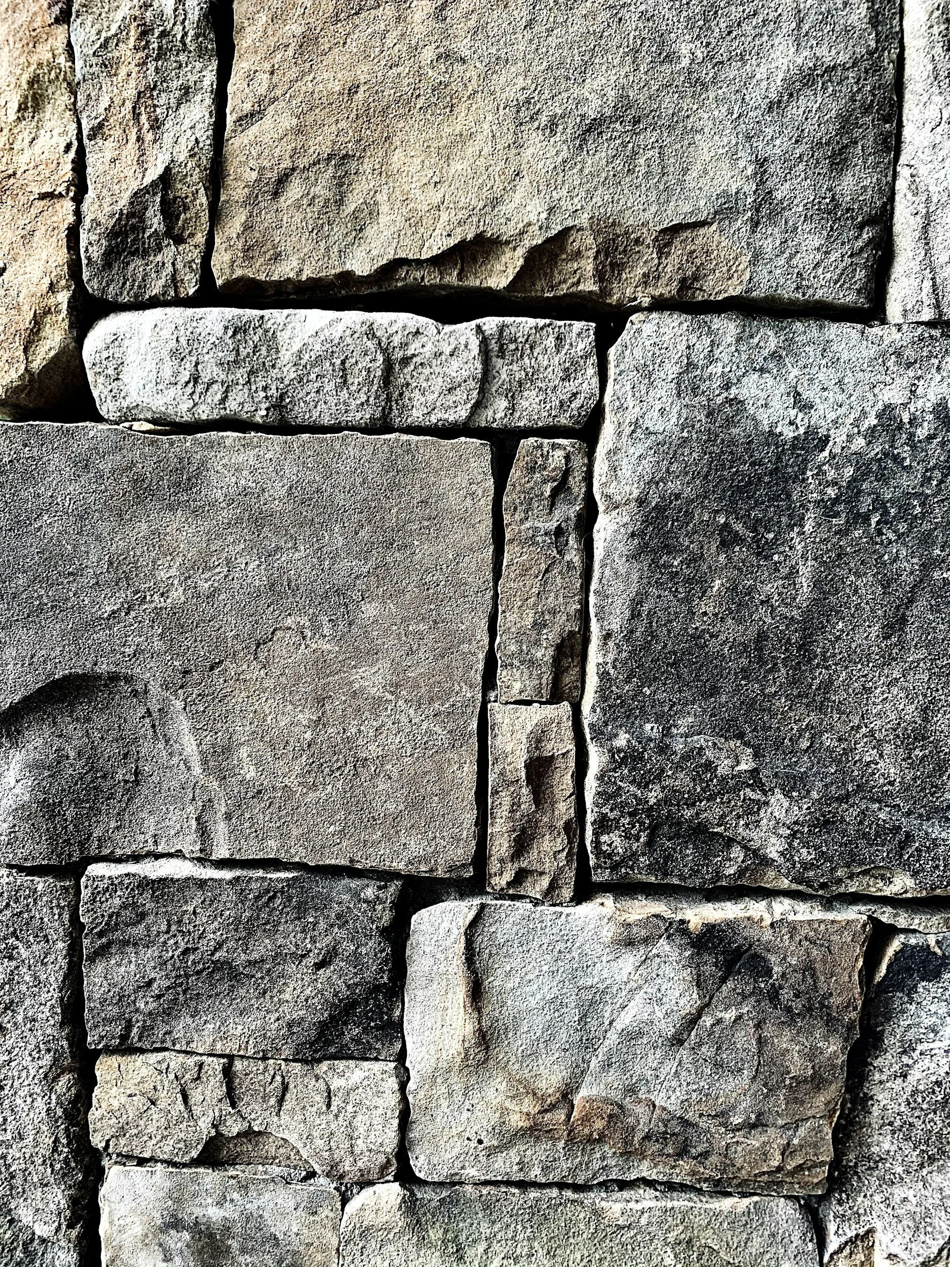 Nahaufnahme einer Steinmauer aus verschieden großen, rauen Steinen in Grau- und Brauntönen.