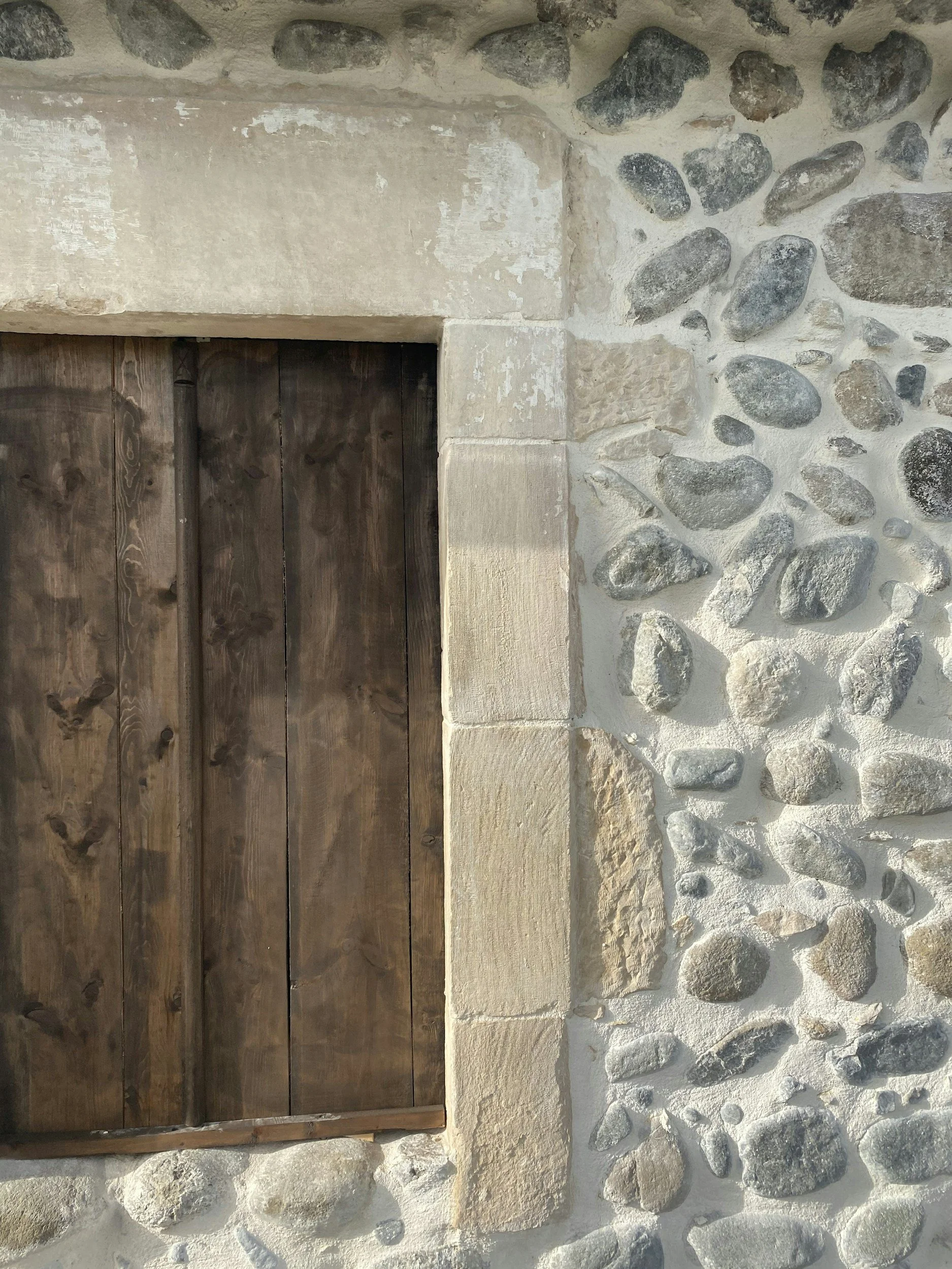 Holztür im Mauerwerksrahmen, umgeben von einer Hauswand aus Kalkstein und Flusssteinen.