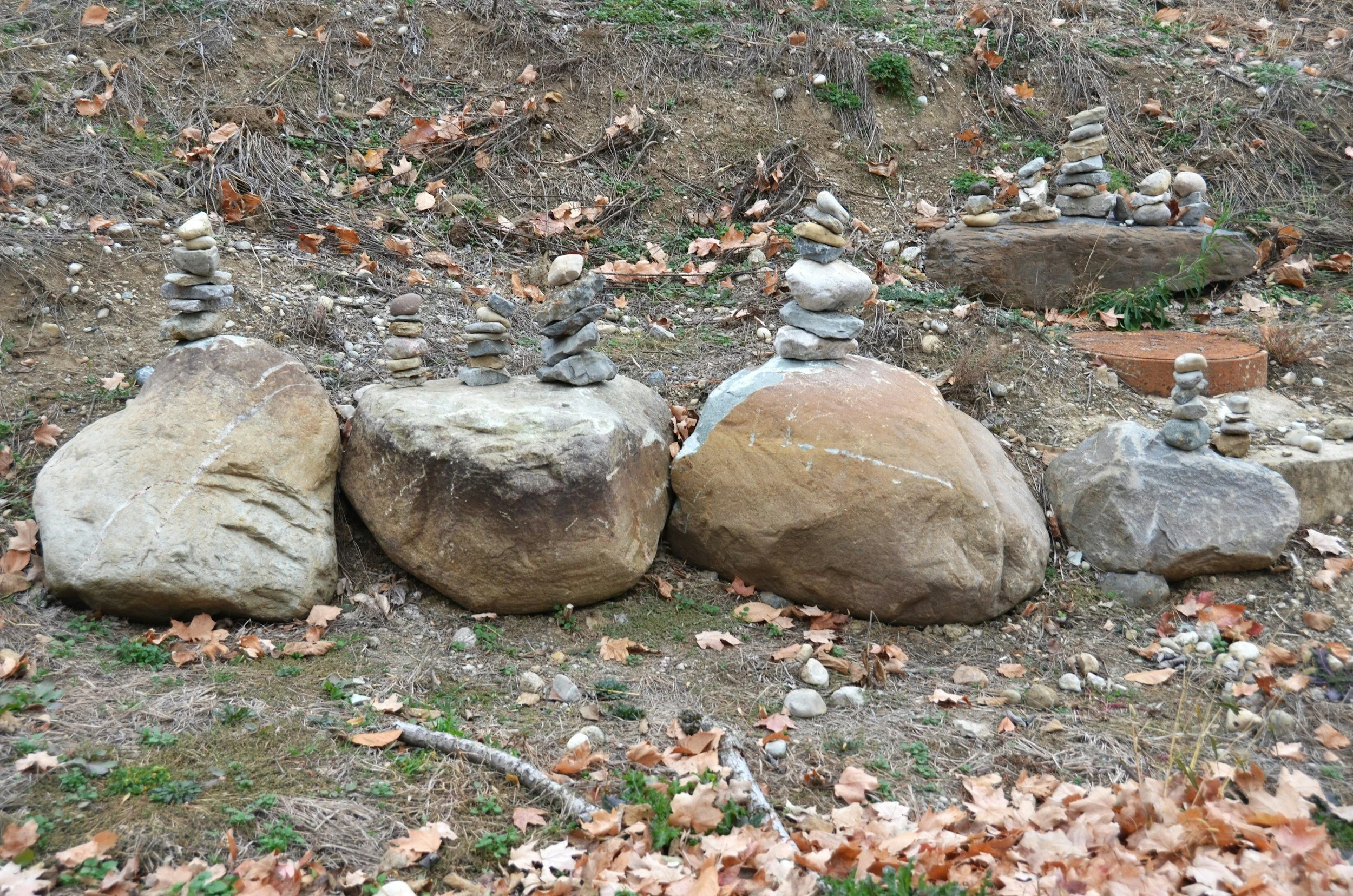 Mehrere große Steine auf dem Boden, mit kleinen Steinen und Sand gefüllt, auf denen gestapelte Steine sind, die wie kleine Türme aussehen.