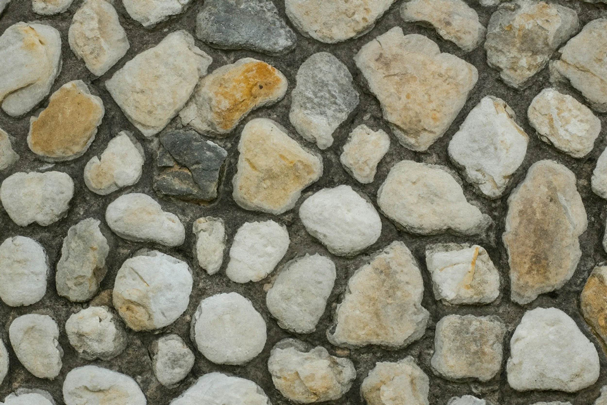 Eine Mauer aus verschiedenen grauen und beigen Steinen, die mit Zement verbunden sind.