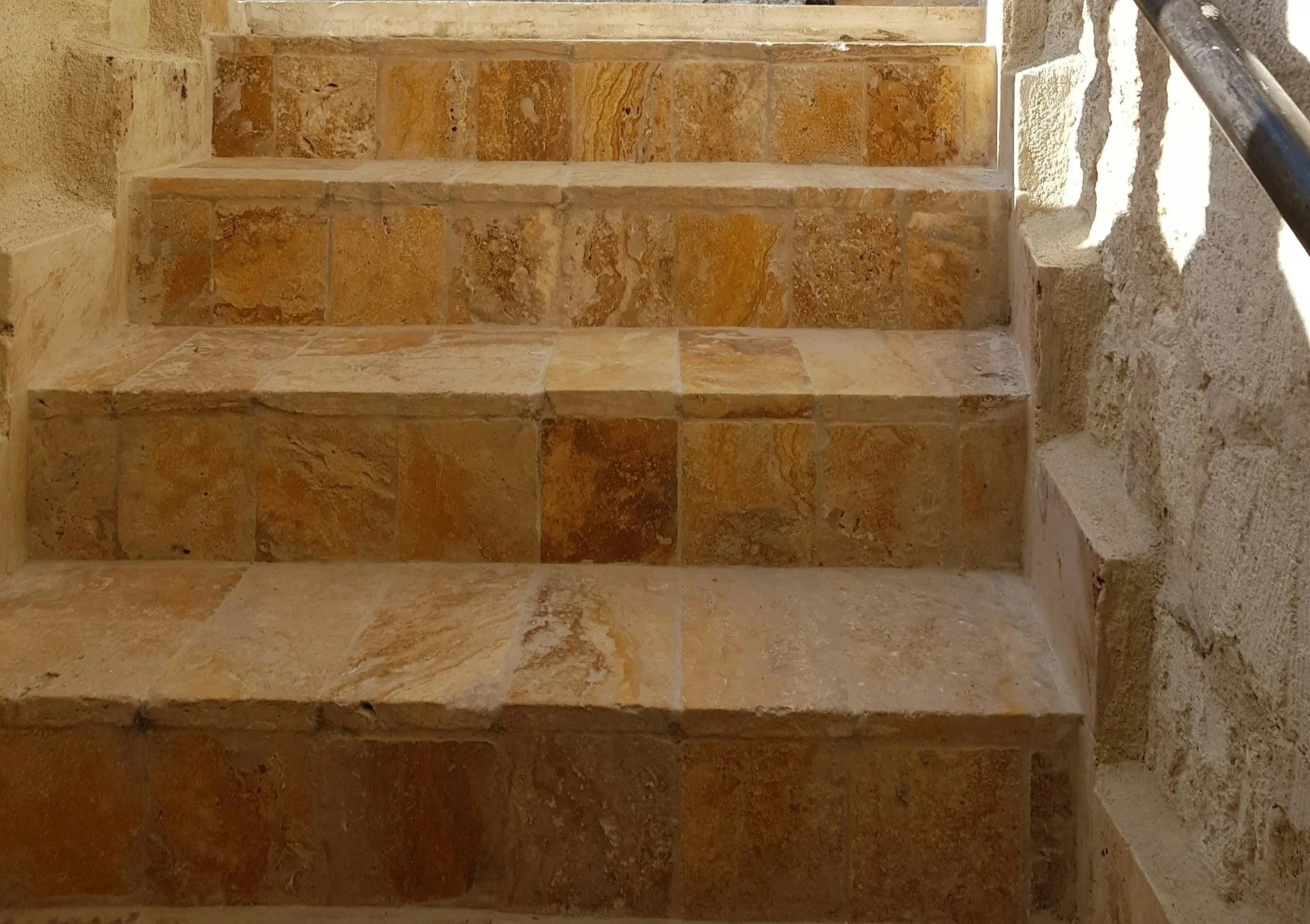 Stufen aus naturfarbenem Stein mit einer dunklen Metallhandlauf an der Seite.