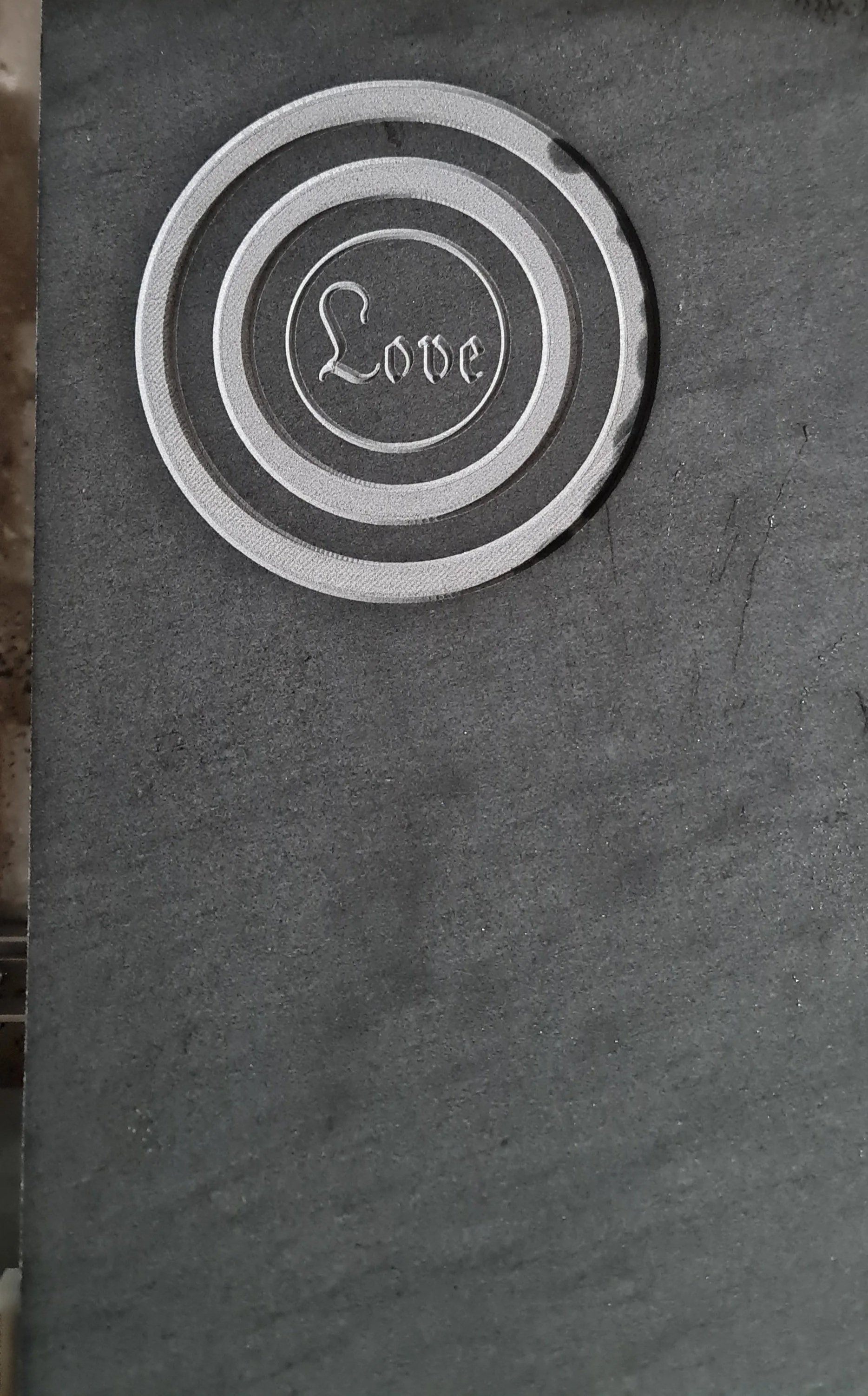 Ein runder Knopf mit dem Wort 'Love' in einer kalligrafischen Schrift, auf einem dunklen, grauen Textur-Hintergrund.