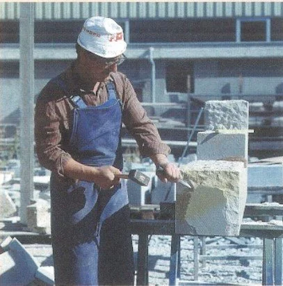 Ein Arbeiter arbeitet mit einem Meißel an einem großen Stein auf einer Baustelle.