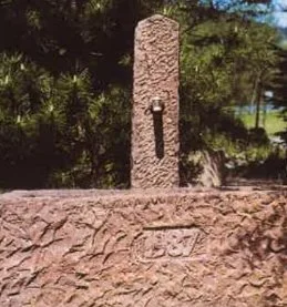 Einen alten Wasserhahn auf einer kleinen Steinmauer mit Bäumen im Hintergrund.