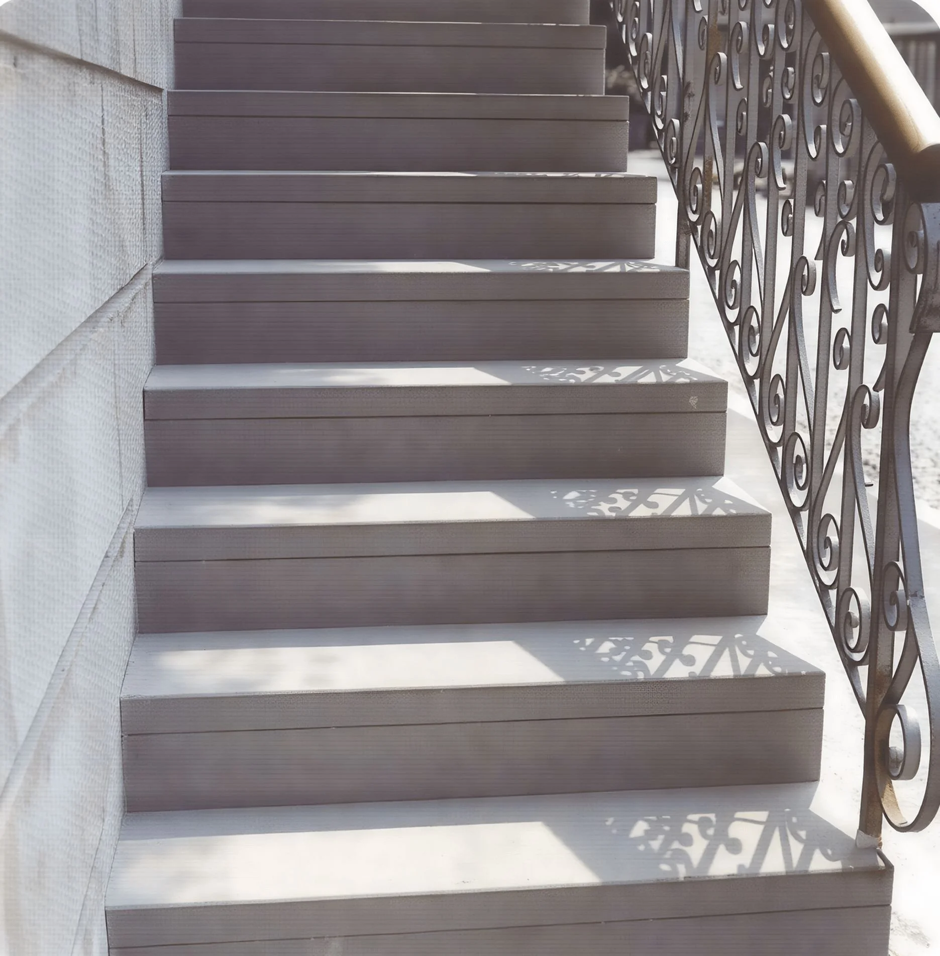 Blick auf eine Außentreppe aus Holz mit einem schmiedeeisernen Geländer, das Schatten wirft.