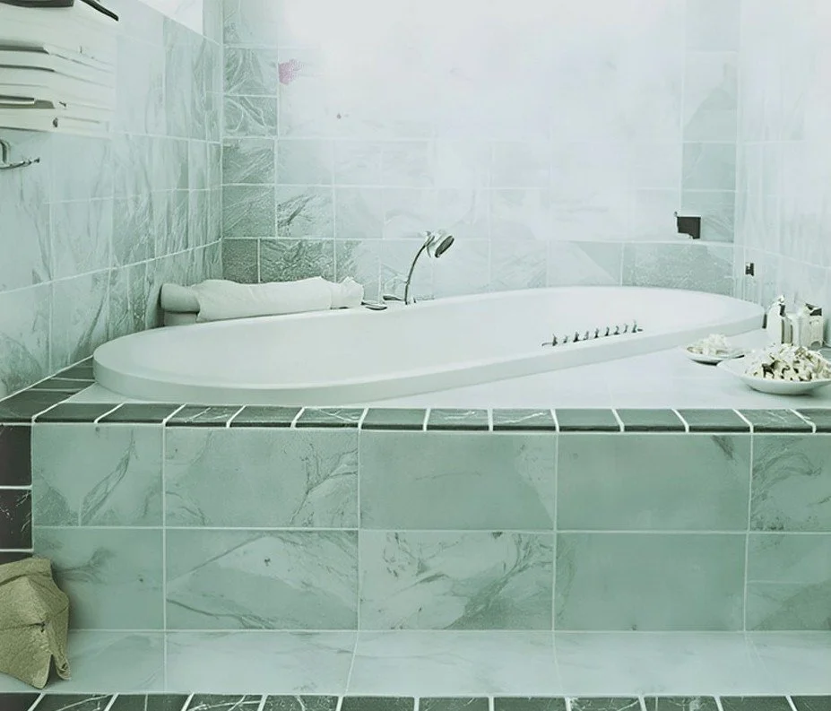Ein weißen Badewanne in einem Badezimmer mit grünen Marmorfliesen, ein Handtuch und Pflegeprodukte auf dem Rand.
