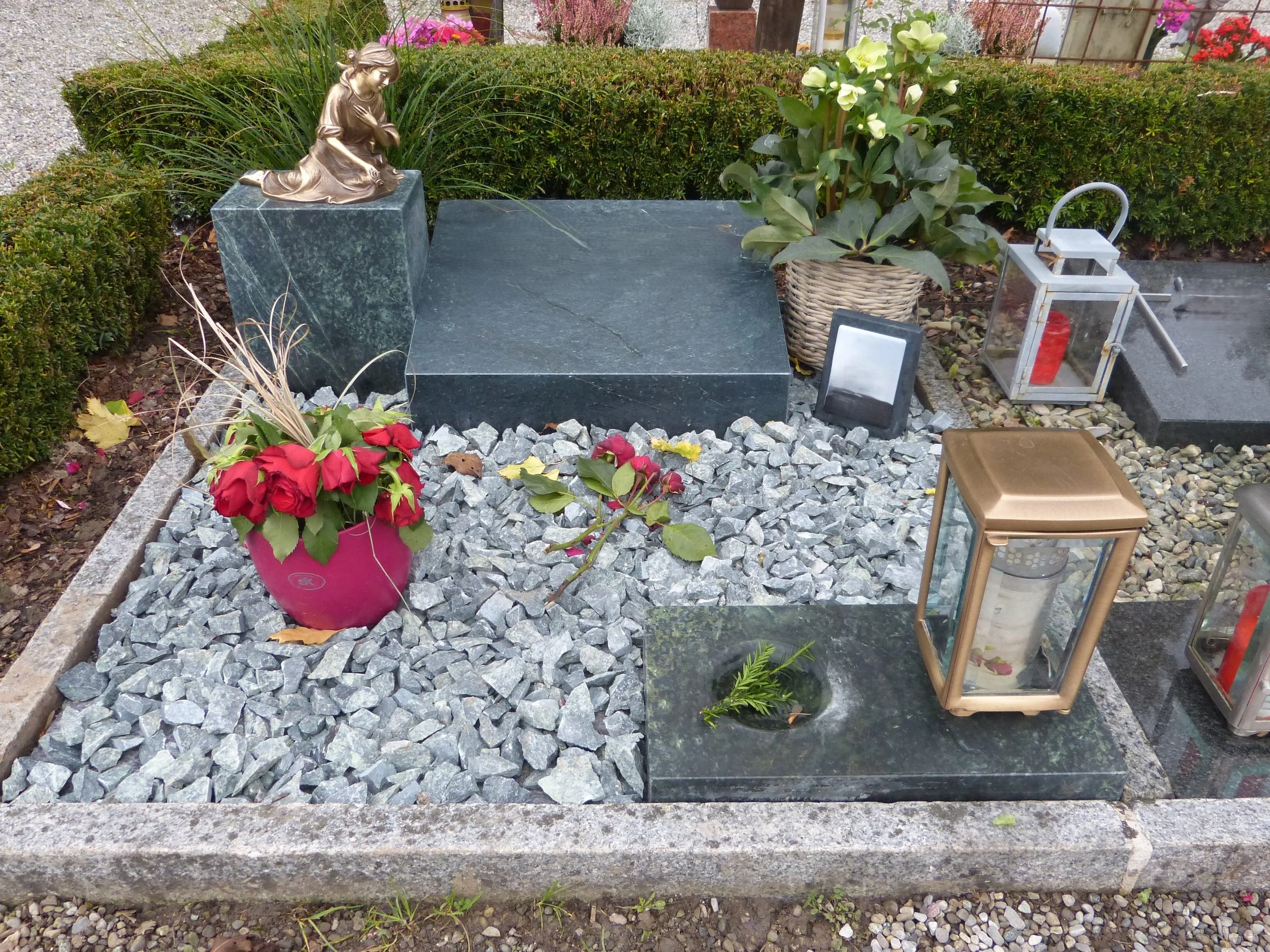 Grabstätte mit Gräbern und Kerzen, Blumen, Laternen und Gedenkobjekten auf einem Friedhof.