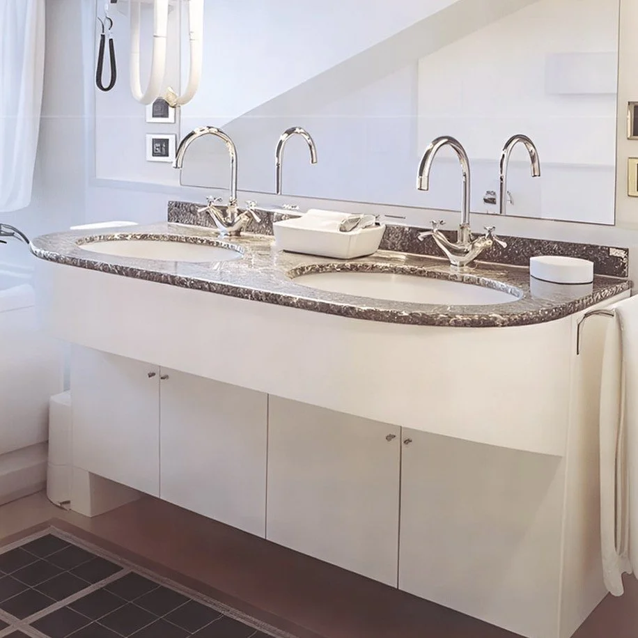 Waschbecken mit zwei Wasserhähnen und Spiegel darüber in einem Badezimmer.