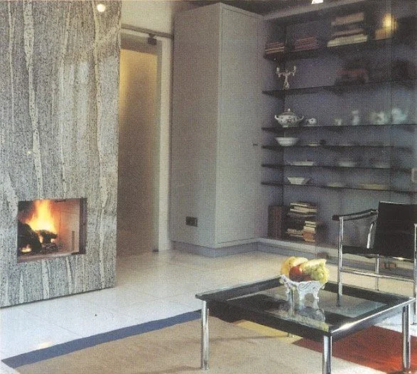 Moderner Wohnraum mit Kamin, Bücherregal, Sessel, Couchtisch mit Dekoration, Teelicht im Hintergrund.