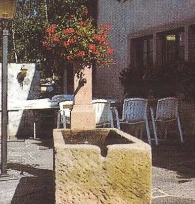 Ein alter, steinerner Wasserschlauch mit getrocknetem Wassergraben, umgeben von Stühlen und Bäumen in einer Stadtstraße.