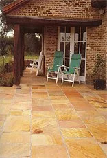 Blick auf eine Terrasse mit bunten Fliesen vor einem Haus mit Backsteinfassade und weißen Fenstern.