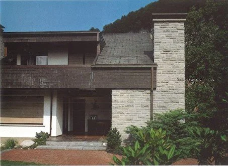 Einfamilienhaus mit moderner Architektur, braunem und weißem Fassaden, umgeben von Grünflächen.