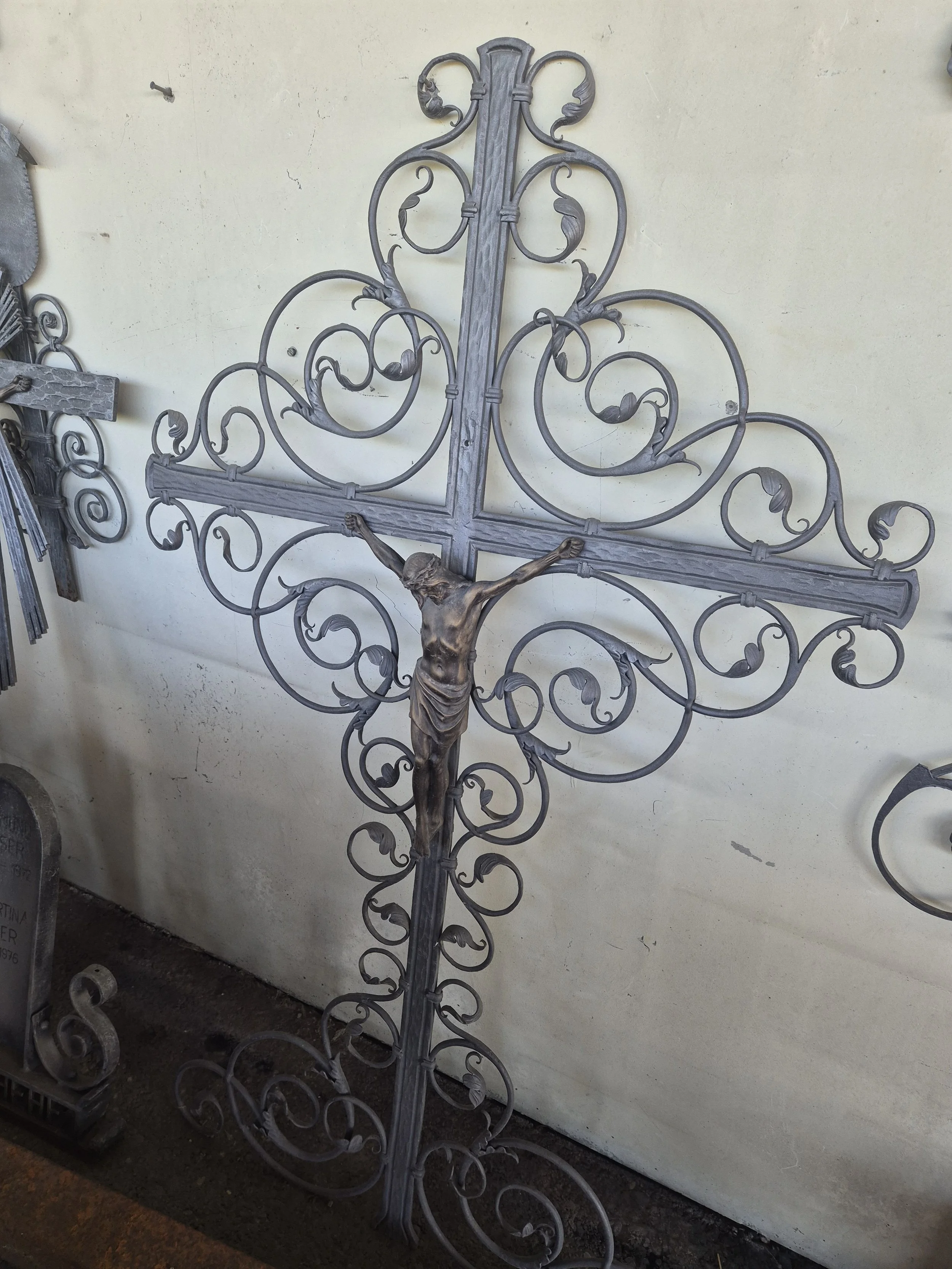 Ein Metallkreuz mit einer Statue von Jesus Christus in der Mitte, umgeben von kunstvollen, geschwungenen Metallverzierungen.