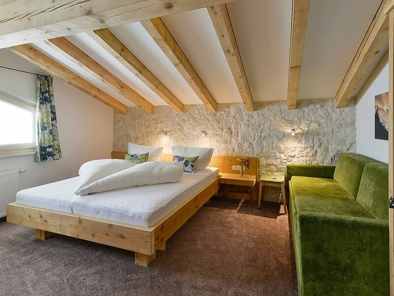 Schlafzimmer mit Doppelbett, grüner Sofa, Holzbalken an der Decke und Steinwand