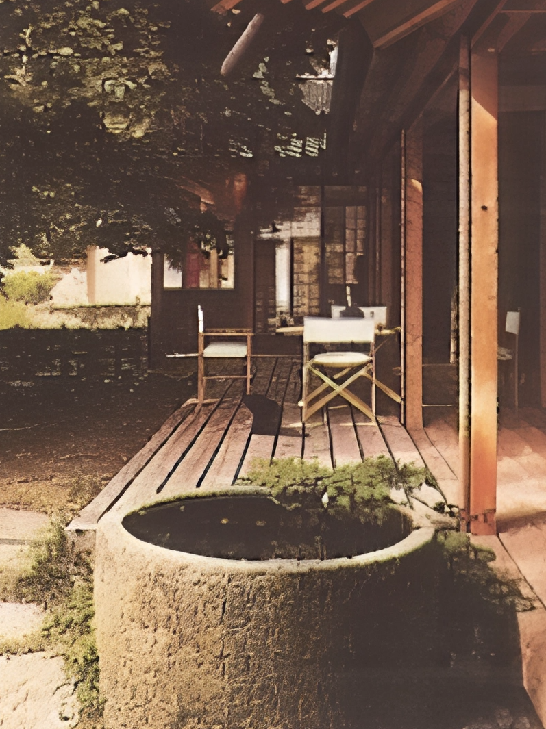 Ein Holzbalkon mit Stühlen und einem großen Pflanzkübel im Garten, umgeben von Bäumen und einem Haus mit Holzverkleidung.