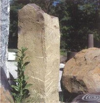 Ein großer, aufrechter Grabstein aus hellem Stein in einem Friedhof, umgeben von Bäumen.