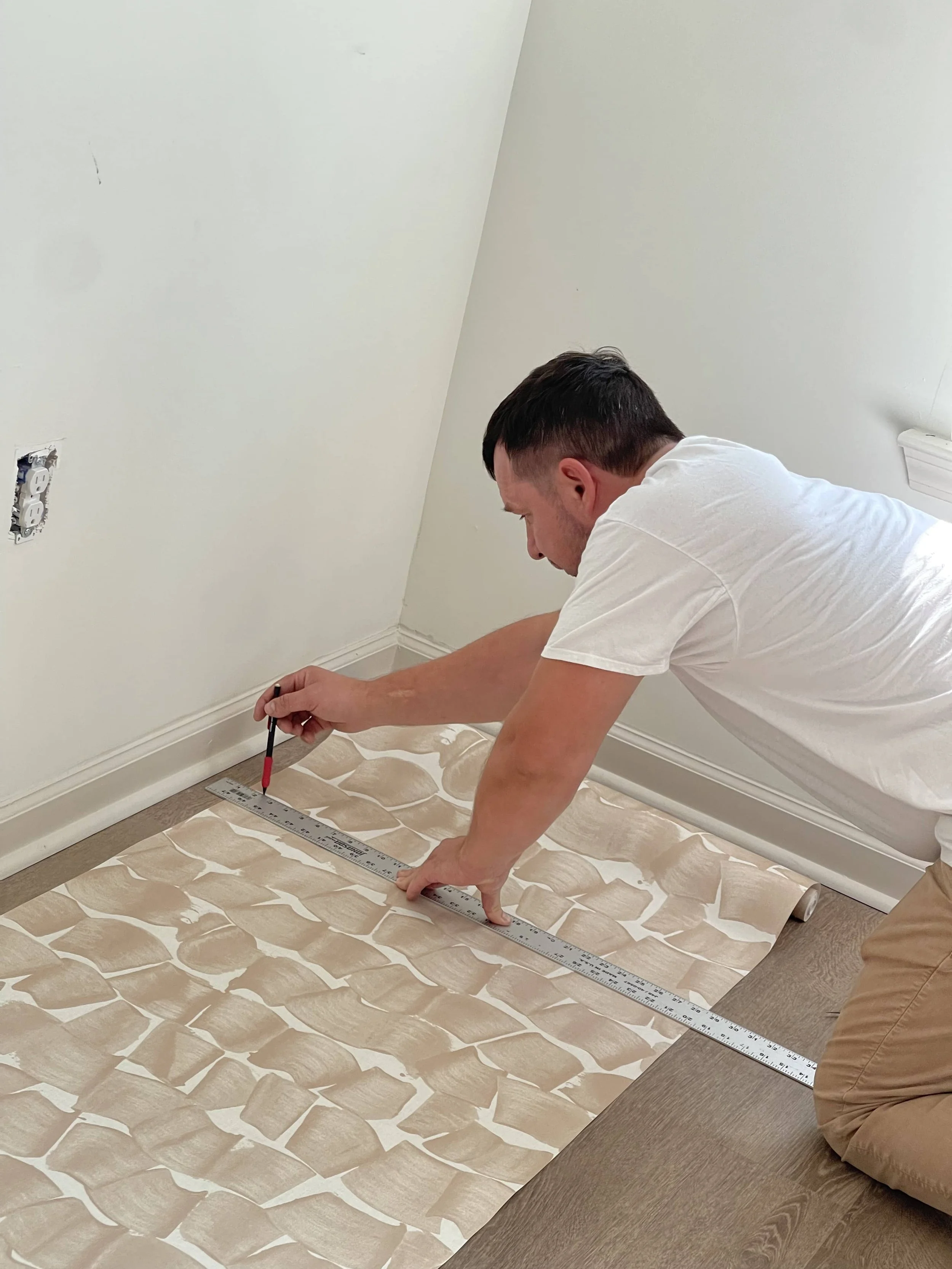 Man measuring and marking patterned wallpaper on the floor in a room under renovation. Wallpaper instalating in Charlotte and near