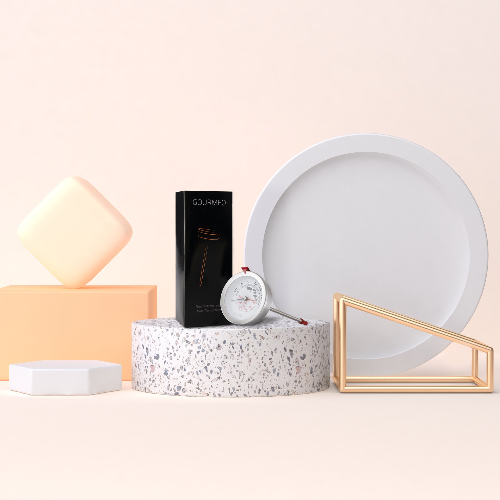 A white round tray, a black box labeled 'GOURMEO', a white and red meat thermometer, various geometric decor with neutral colors, including a peach-colored rectangular block, a white hexagon, a small white round dish, a cream-colored square with a ro