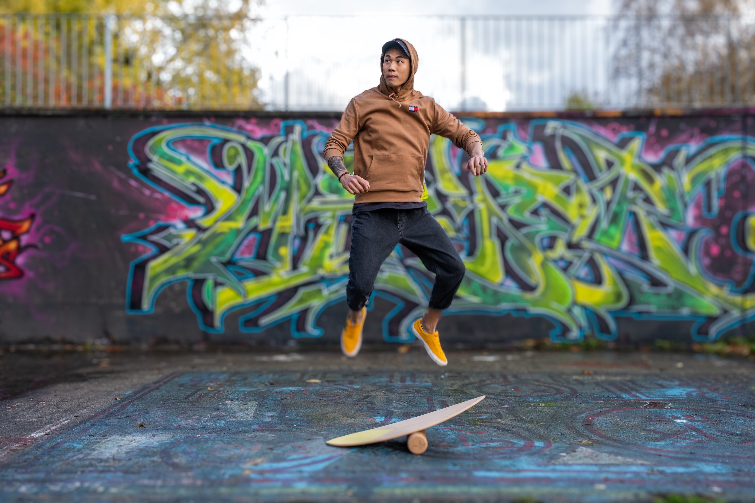 Person jumping on skateboard at an outdoor skate park with graffiti art background.
