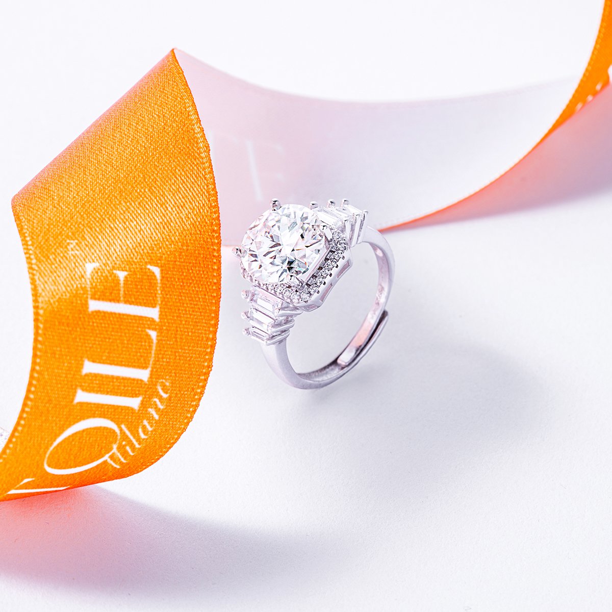 A diamond ring with a large round center stone and smaller diamonds along the band, next to an orange Tiffany & Co. ribbon.