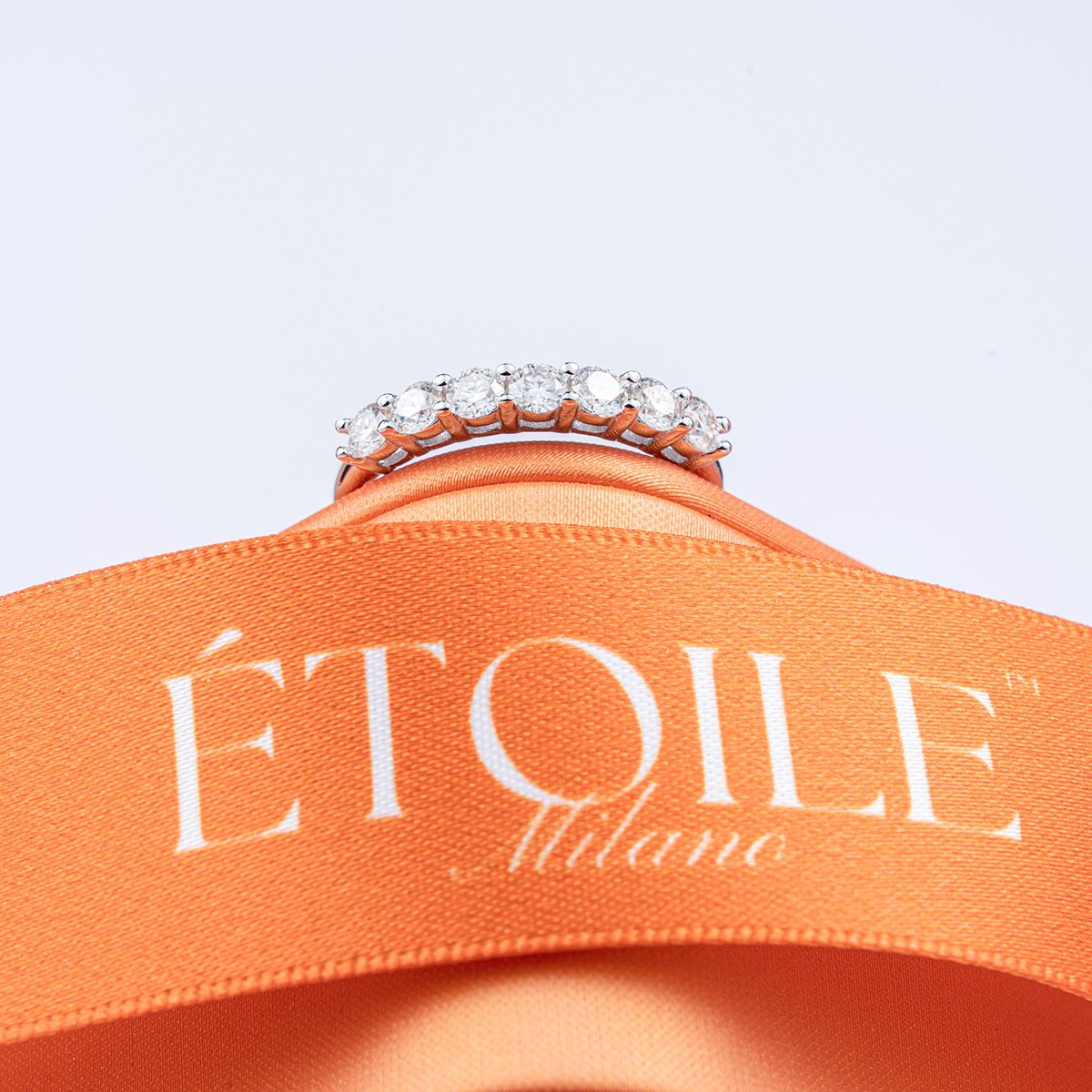 A ring with multiple diamonds on a pink band resting on an orange fabric with the words 'L'ÉTOILE Détente' printed on it.