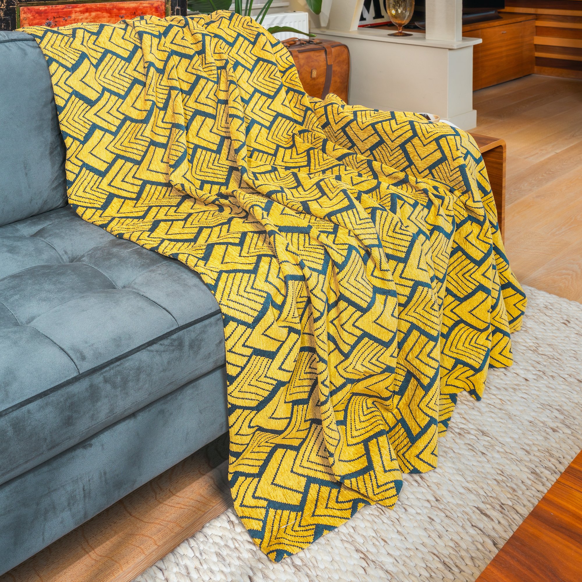 A yellow and blue geometric patterned blanket draped over a light blue velvet sofa in a living room.